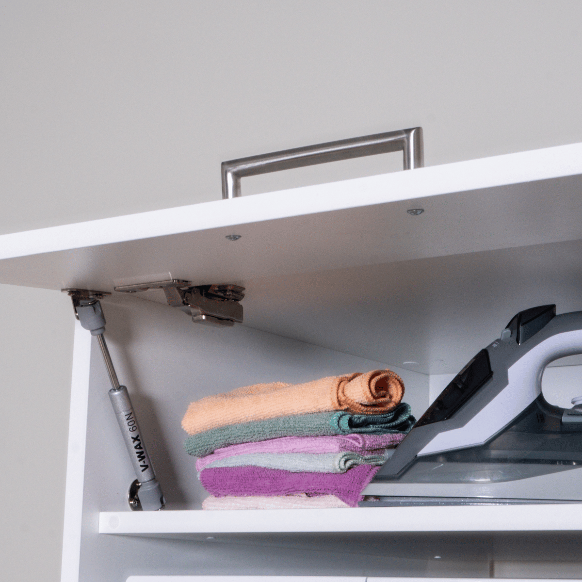 White cabinet interior with three folded pastel towels and a modern iron on the right side.